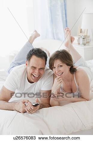 "Mature couple watching TV in bed, smiling" View Large Photo Image Stock Image - "Mature couple watching TV in bed, smiling". Fotosearch