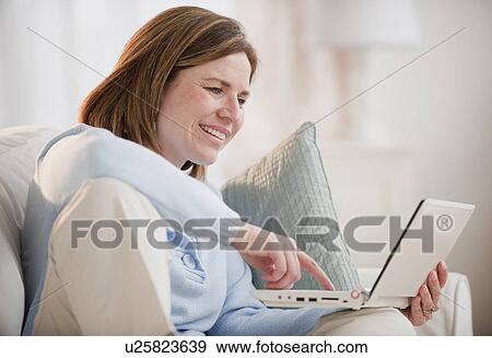 Stock Photo - Mature woman using laptop on sofa. Fotosearch