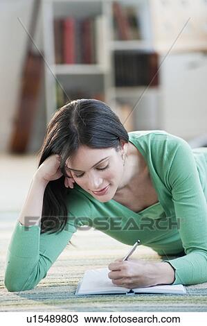 Stock Image - Mid-adult woman lying on floor and writing. Fotosearch