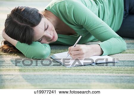 Stock Image - Mid-adult woman lying on floor and writing. Fotosearch
