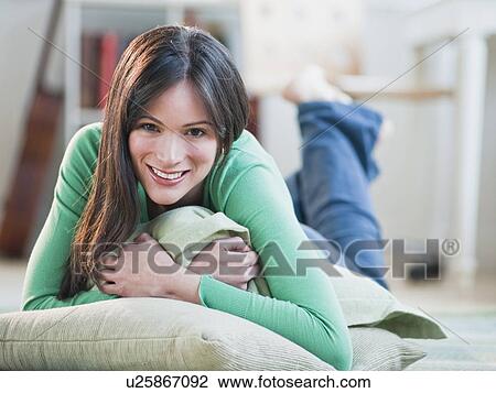 Stock Image - Mid-adult woman lying on floor hugging blanket. Fotosearch