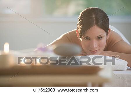Stock Image - Mid-adult woman lying on massage table with candles and rocks in foreground. Fotosearch