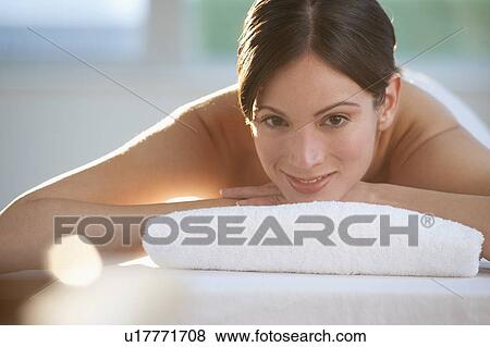 Stock Photo - Mid-adult woman lying on massage table with candle in foreground. Fotosearch