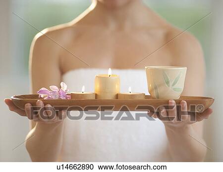 Stock Image - Mid-adult woman wearing towel carrying candles on tray. Fotosearch