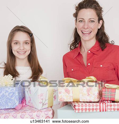 Stock Image - "Mother and daughter (10-12 years) with stack of presents, smiling, portrait". Fotosearch
