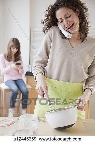"Mother preparing food while talking on the phone, daughter (10-12 years) in background" View Large Photo Image Stock Photo - "Mother preparing food while talking on the phone, daughter (10-12 years) in background". Fotosearch