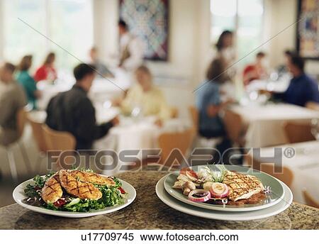 Stock Photography - "Plates with food on bar counter in restaurant, people in background". Fotosearch