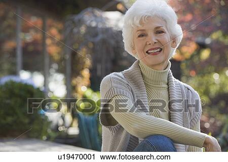 Stock Image - Portrait of senior woman sitting in garden. Fotosearch