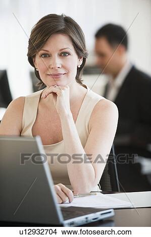 Portrait of successful mature businesswoman sitting by desk in office View Large Photo Image Picture - Portrait of successful mature businesswoman sitting by desk in office. Fotosearch