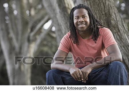 Stock Photo - "Portrait of teenage boy (16-17) with dreadlocks, sitting in park". Fotosearch