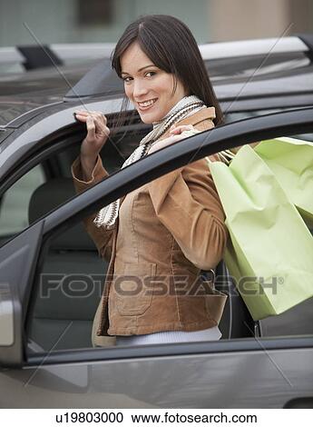 Stock Image - Portrait of woman getting into car with shopping bags. Fotosearch