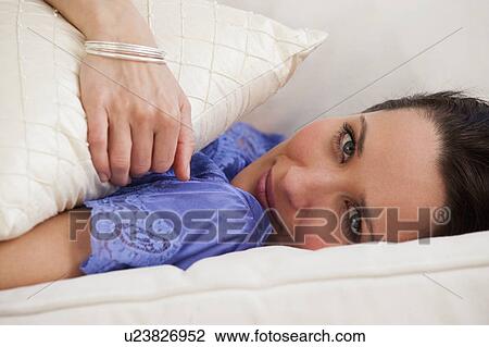 Stock Image - Portrait of woman lying on bed. Fotosearch