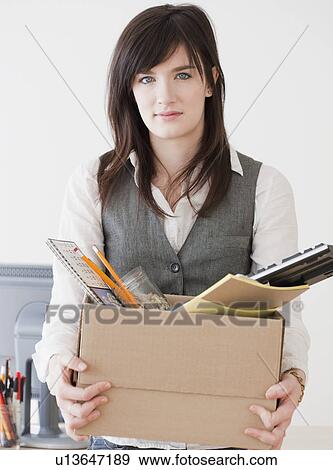 Stock Photo - Portrait of young woman carrying office supplies in box. Fotosearch