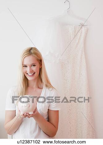 Stock Image - Portrait of young woman holding piggy bank with savings for wedding. Fotosearch