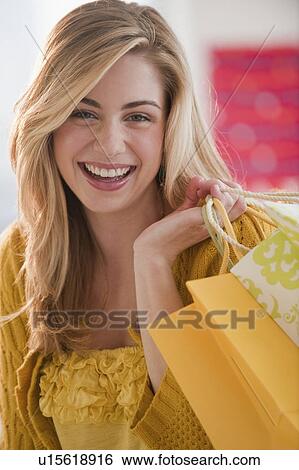 Stock Photograph - Portrait of young woman holding shopping bags in shop. Fotosearch