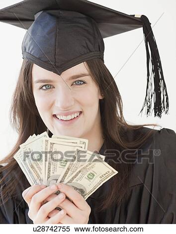 Stock Photography - Portrait of young woman in graduation gown holding dollars. Fotosearch