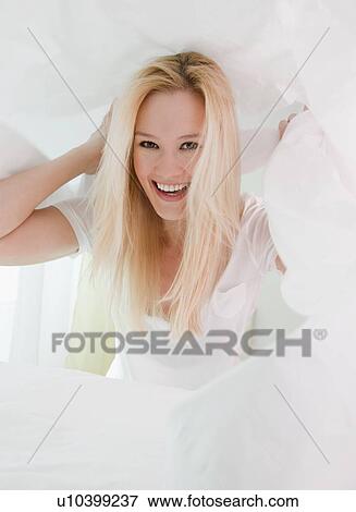 Stock Photo - Portrait of young woman messing about under pristine white pillows. Fotosearch