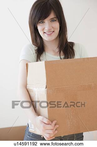 Stock Image - Portrait of young woman moving to new house and holding cardboard box. Fotosearch