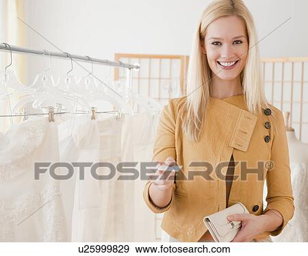 Stock Photo - Portrait of young woman paying for wedding dress in bridal shop. Fotosearch