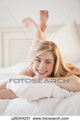 Stock Image - Portrait of young woman relaxing on bed. Fotosearch