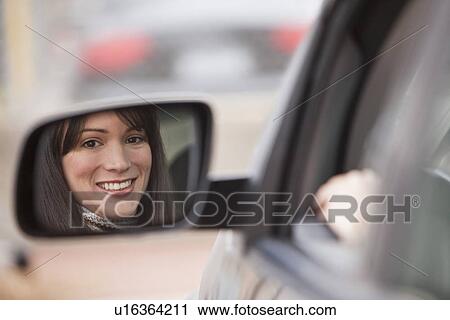 Stock Image - Reflection of woman in side view mirror. Fotosearch