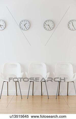 Stock Photography - Row of chairs in waiting room under clocks displaying time zones. Fotosearch