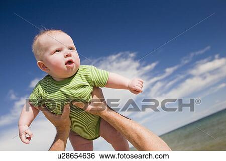 Stock Photograph - "Senior man lifting baby in air, Beaver Island, Michigan, USA". Fotosearch