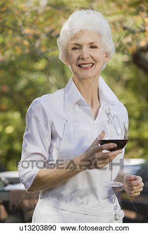 Stock Image - "Senior woman holding glass of red wine, portrait". Fotosearch