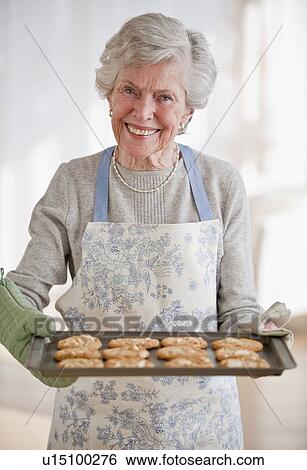 Stock Photograph - Senior woman holding tray with baked cookies. Fotosearch