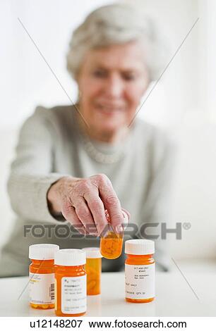 Stock Photo - Senior woman picking up pill bottle. Fotosearch