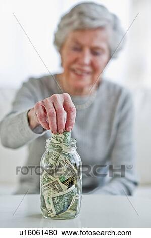 Senior woman putting banknote into money jar View Large Photo Image Stock Image - Senior woman putting banknote into money jar. Fotosearch