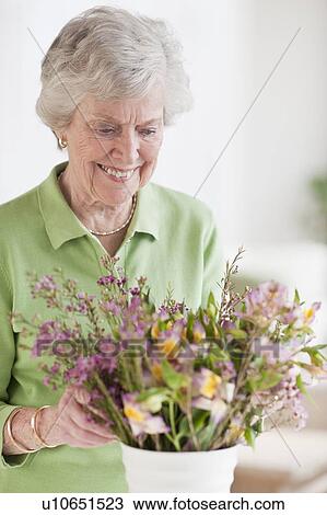 Stock Image - Senior woman setting flowers in vase. Fotosearch