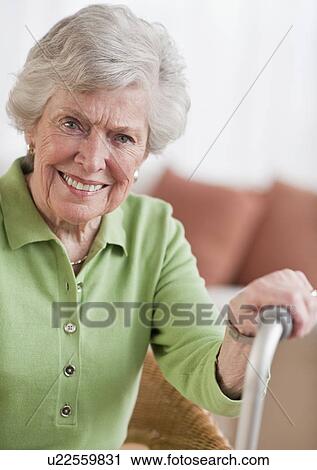 Stock Image - Senior woman sitting and holding walking stick. Fotosearch