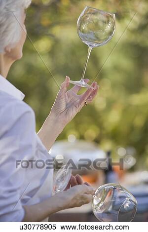 Stock Photography - Senior woman standing in garden and examining wineglasses. Fotosearch