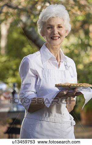 Senior woman standing in garden holding pie View Large Photo Image Stock Image - Senior woman standing in garden holding pie. Fotosearch