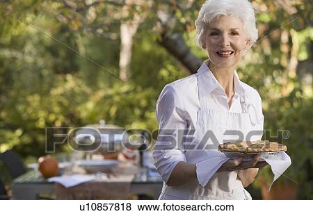 Senior woman standing in garden holding plate with pie View Large Photo Image Stock Photo - Senior woman standing in garden holding plate with pie. Fotosearch