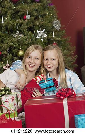 Sisters sitting in front of Christmas tree and holding Christmas gifts View Large Photo Image Stock Image - Sisters sitting in front of Christmas tree and holding Christmas gifts. Fotosearch