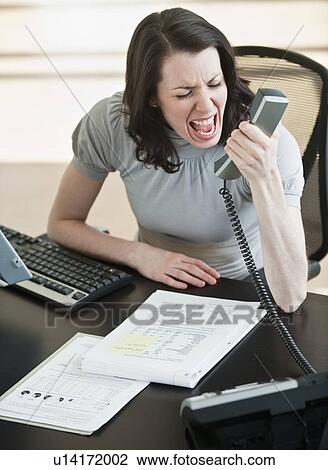 Stock Image - Stressed business woman using telephone in office. Fotosearch