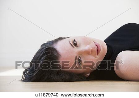 Stock Image - Studio portrait of woman lying on floor. Fotosearch