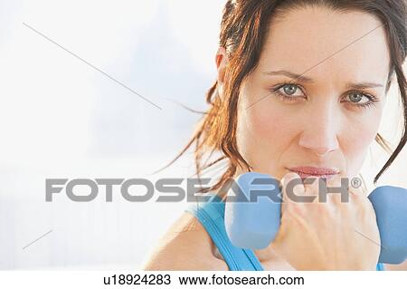 Stock Image - Studio portrait of woman using dumbbell. Fotosearch