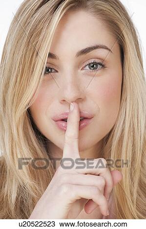 Stock Image - Studio portrait of young woman with finger to lips. Fotosearch