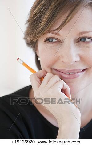 Stock Image - Successful mature businesswoman holding pencil and smiling. Fotosearch