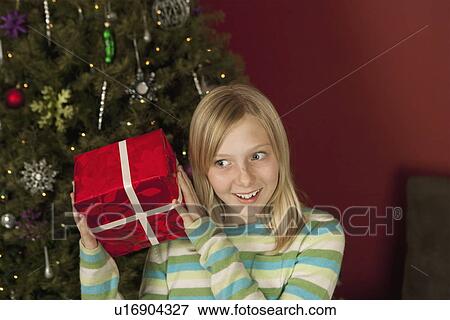 Teenage girl (10-12) shaking Christmas gift View Large Photo Image Stock Photo - Teenage girl (10-12) shaking Christmas gift. Fotosearch