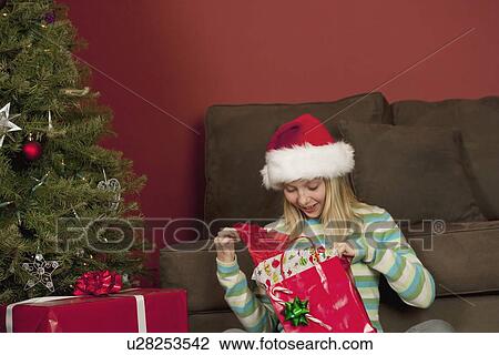 Stock Image - Teenage girl (13-15) wearing Santa hat opening Christmas gift. Fotosearch