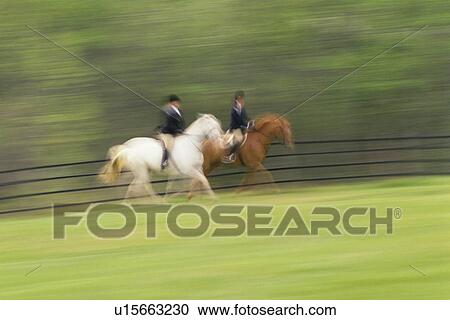 Stock Image - "Two people riding on horses on field, blurred motion". Fotosearch