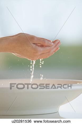 Stock Photograph - Water dripping from cupped hands over bowl. Fotosearch