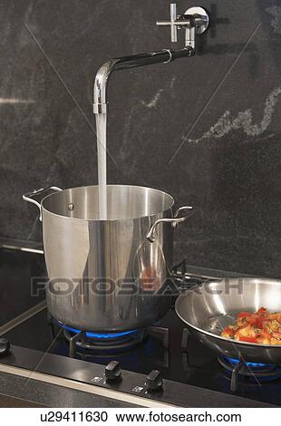 Stock Image - Water pouring from tap into pot. Fotosearch