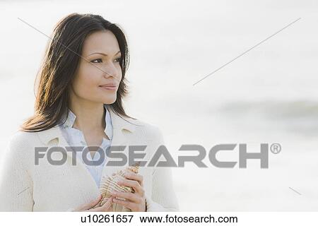 Stock Photo - Woman holding shell by sea. Fotosearch