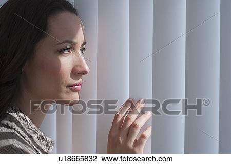 Stock Image - Woman looking through blinds. Fotosearch
