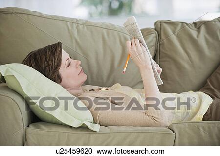 Stock Image - Woman lying on sofa with newspaper. Fotosearch